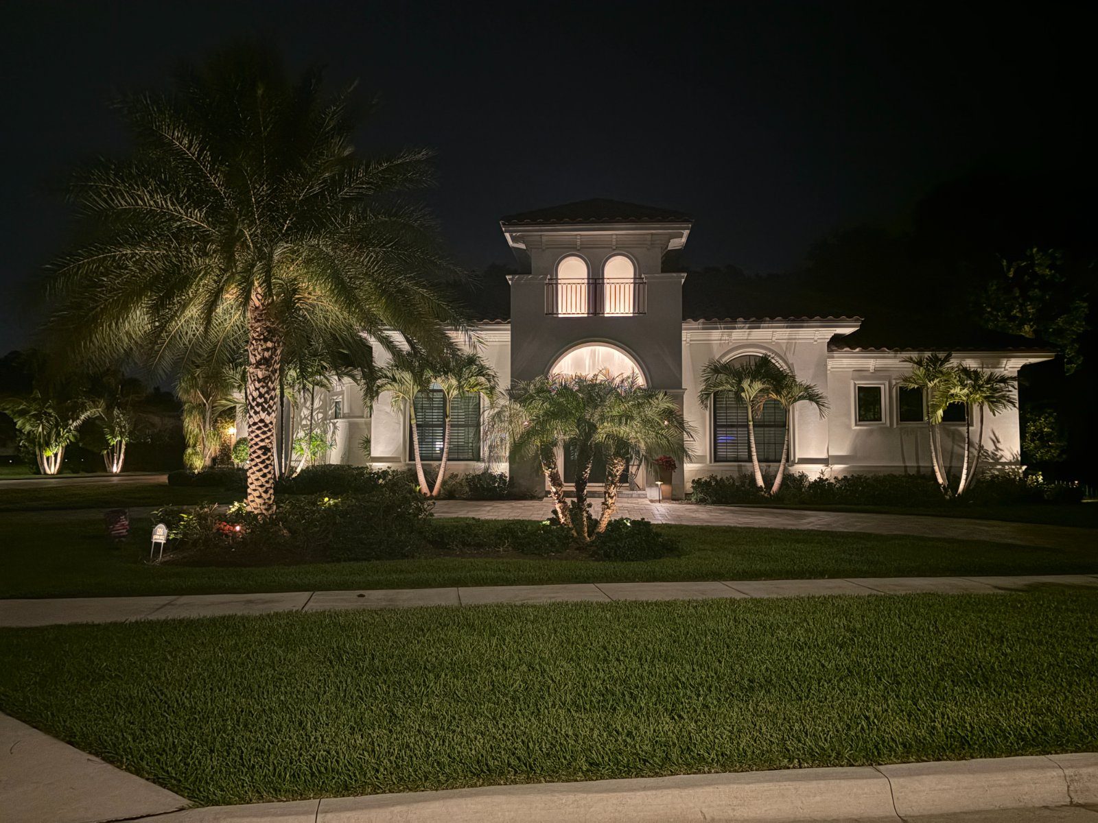 Tampa Bay home at night with uplit palms, a lit entry tower, and warm landscape lighting across the facade, a real LogiBuilt install