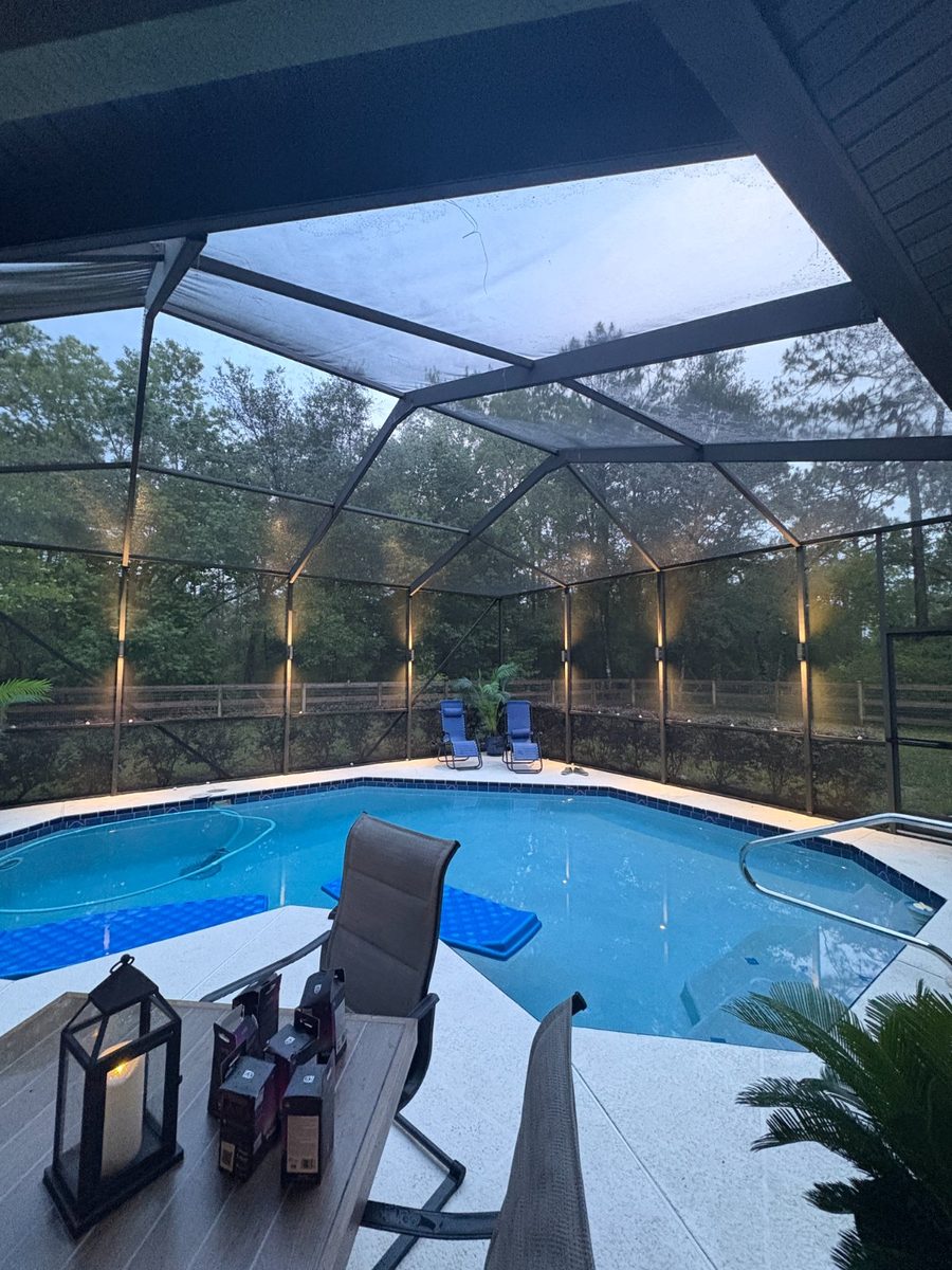 Pool cage at dusk with warm sconces on every post and the pool lit